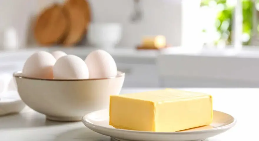 Schüssel mit Eiern und Butter auf einem Teller. Die Frage bei welcher Temperatur stockt Ei wird hier nicht beantwortet.