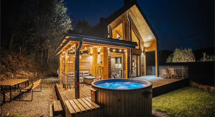 Drewniany domek z jacuzzi i tarasem, idealne miejsce na babia góra noclegi. Oświetlony girlandami, zaprasza do relaksu.