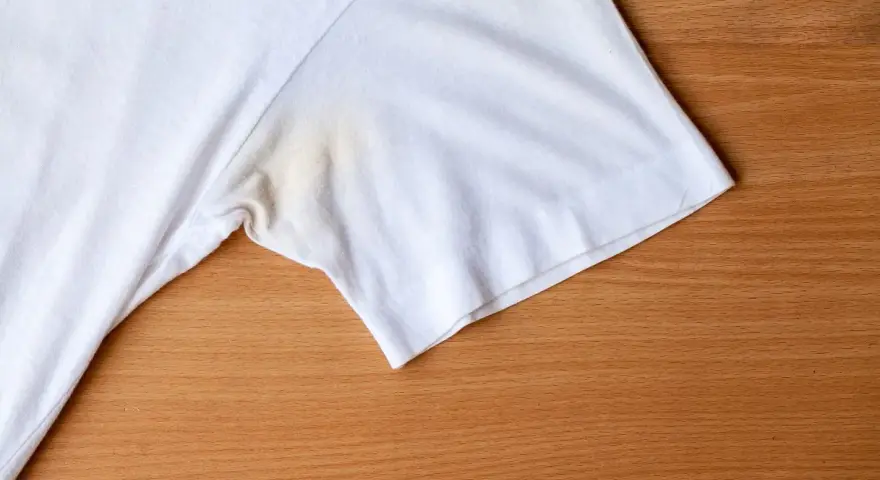 T-shirt blanc avec une tache de transpiration incrustée sous le bras, sur fond de bois.