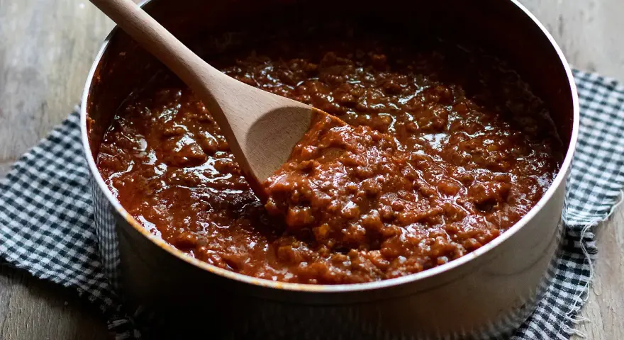 Un pentolino pieno di profumato ragù di carne, pronto per condire la pasta. Un cucchiaio di legno mescola la salsa densa e invitante.