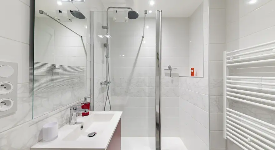 Salle de bain moderne, prête pour la prochaine étape de rénovation. Douche, lavabo et sèche-serviettes blancs.