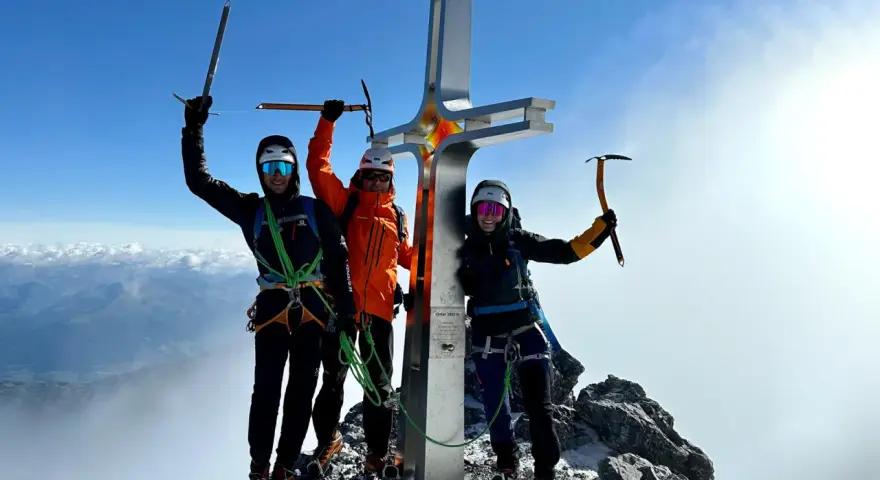 Drei Bergsteiger feiern am Gipfelkreuz des Ortler Normalwegs ihren Erfolg.