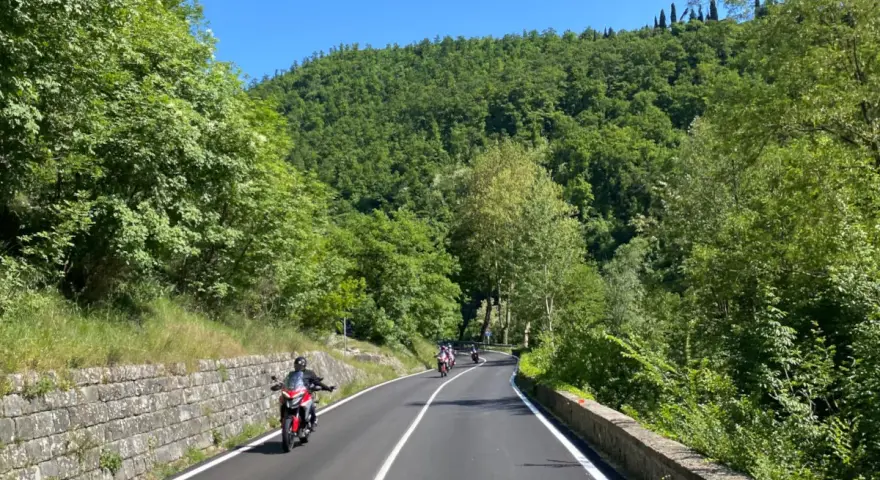 Motociclisti su strade panoramiche in Emilia Romagna, tra colline verdi e cielo azzurro.
