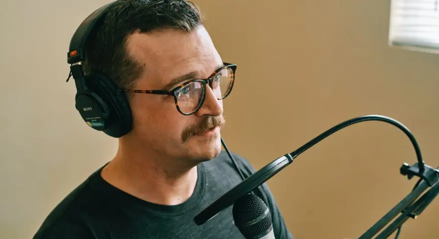 Mężczyzna w okularach i słuchawkach Sony nagrywa podcast. Dba o odpowiedni gain staging, by dźwięk był czysty.