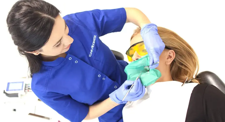 Dentystka zakłada koferdam pacjentce, przygotowując ją do zabiegu.