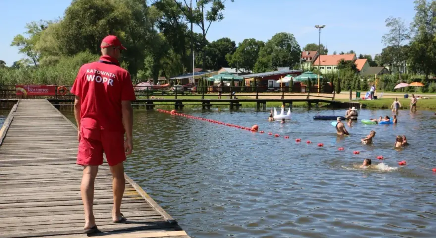 Ratownik WOPR czuwa nad bezpieczeństwem kąpiących się na Jeziorze Skępe. Ludzie pływają i relaksują się w wodzie.