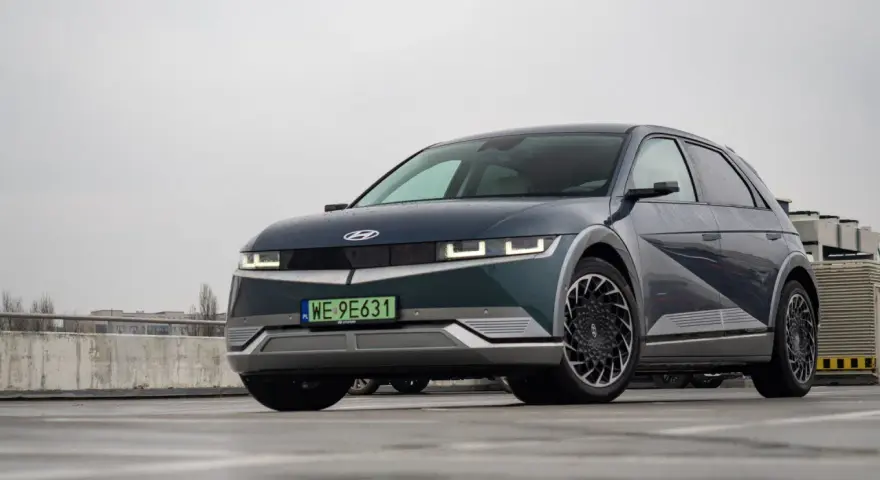 Hyundai Ioniq 5, z charakterystycznymi światłami i felgami, prezentuje swoje imponujące wymiary na mokrym parkingu.