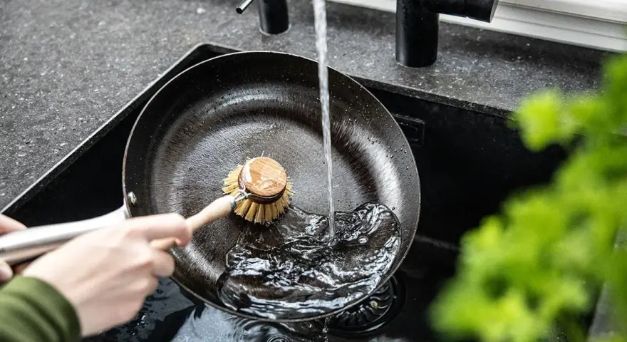Mycie patelni żeliwnej pod bieżącą wodą za pomocą szczotki.