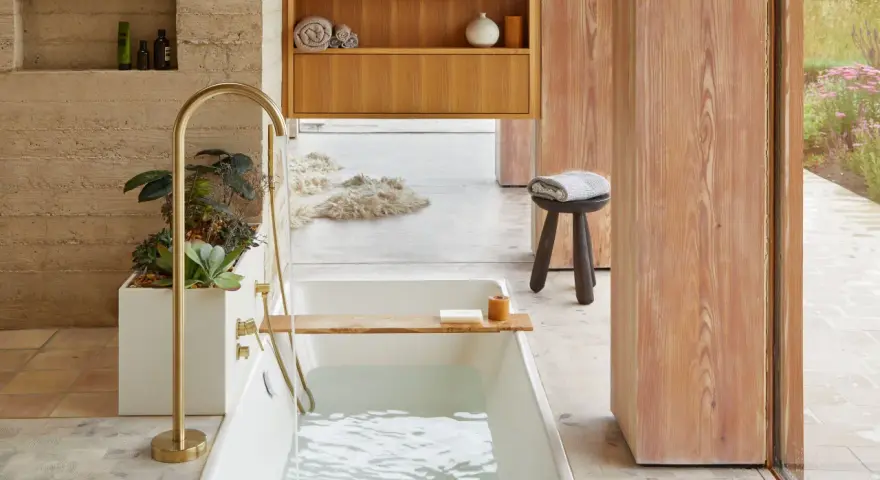 Bain relaxant avec baignoire remplie, robinetterie dorée, plantes et bois. Une belle inspiration salle de bain.