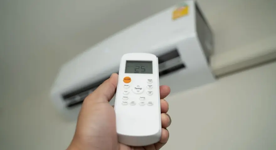 Dłoń trzymająca pilot do klimatyzatora, ustawiająca temperaturę 25°C. Ogrzewanie klimatyzatorem to komfort.