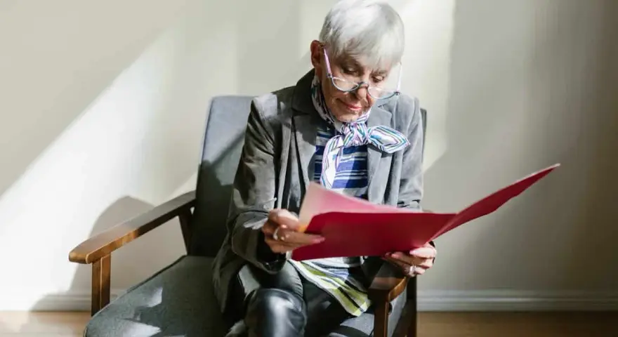 Une femme âgée, en pleine retraite, examine des documents artistiques dans un dossier rouge.