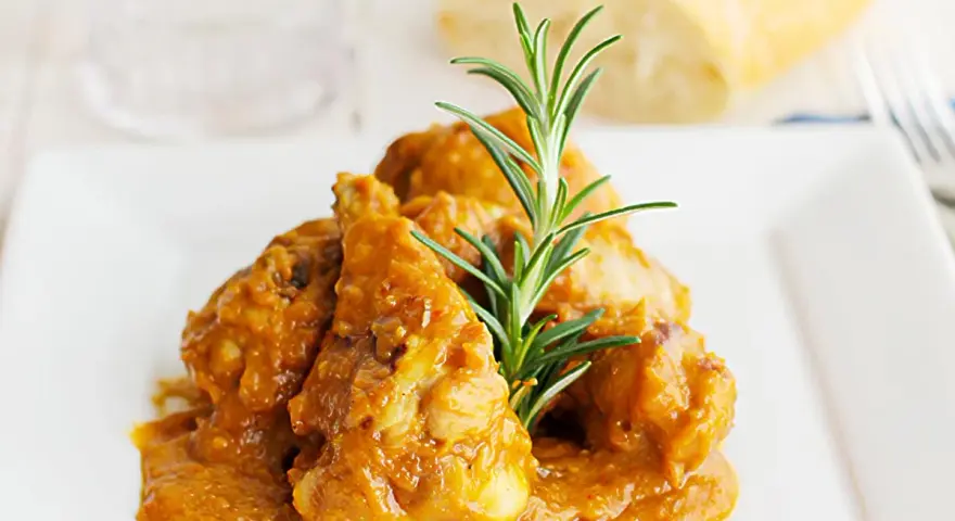Sabroso pollo con almendras en una salsa dorada, adornado con romero fresco. Un plato que invita a disfrutar.
