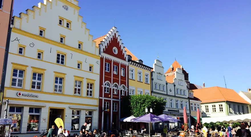 Bunte Häuserfronten säumen den mv markt. Menschen sitzen in Cafés unter Sonnenschirmen und genießen den sonnigen Tag.
