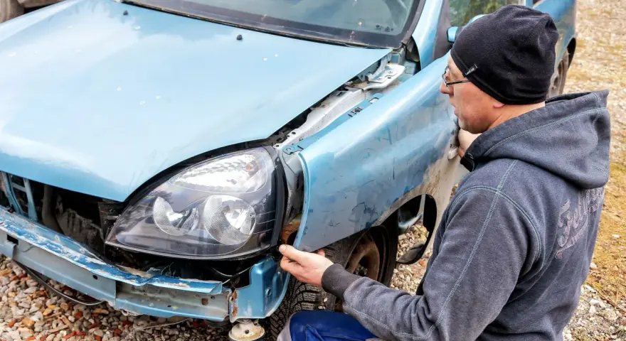 Mężczyzna w czapce i bluzie naprawia niebieską ćwiartkę samochodu, która ucierpiała w wypadku.