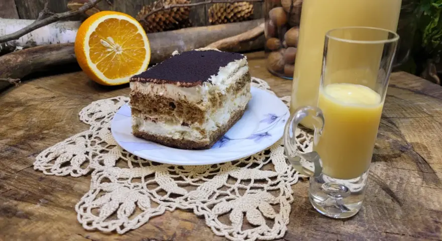 Słodki deser tiramisu, połówka pomarańczy i kieliszek likieru ze skórek pomarańczy na drewnianym blacie.