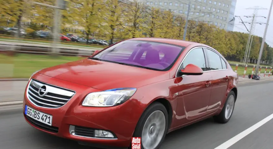 Czerwony Opel Insignia 1.6 Turbo w ruchu ulicznym. Wady tego modelu mogą dotyczyć np. spalania.