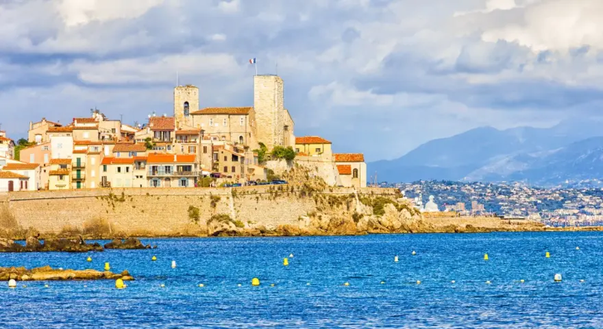 Vista de la ciudad amurallada de Antibes, Francia, con sus torres y edificios coloridos sobre un acantilado, bañada por el mar azul.