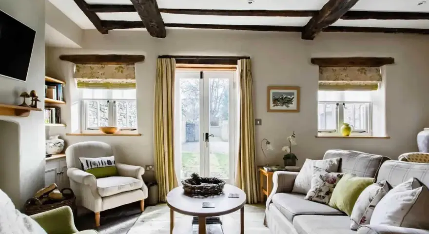 Salon confortable d'un maison cottage anglais, avec poutres apparentes, fauteuils douillets et vue sur le jardin.