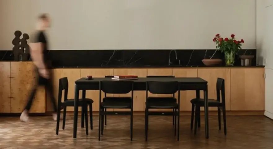 Jadalnia z czarnym stołem i krzesłami, otoczona meblami w ciepłych odcieniach dębu. W tle bukiet czerwonych róż.