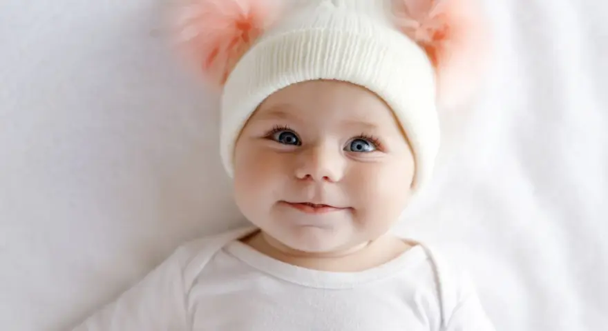 Ein süßes Baby mit blauen Augen und einer Mütze mit Bommeln. Man fragt sich, welche Augenfarbe bekommt mein Kind.