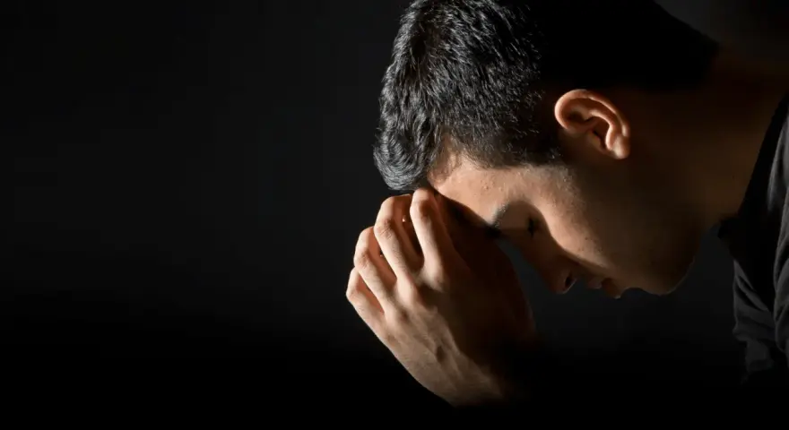 A man bows his head in prayer, hands clasped, reflecting the repentance meaning in the bible.