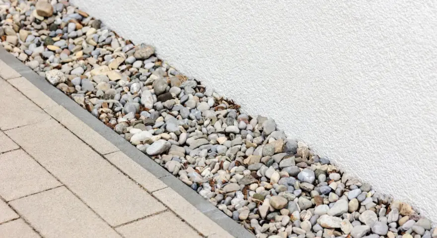 Kiesbett als Spritzschutz am Haus, neben gepflastertem Weg.