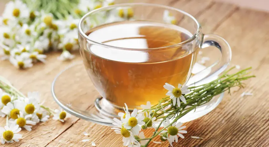Une tasse de tisane de camomille, idéale pour le rhume traitement, entourée de fleurs fraîches sur un fond en bois.
