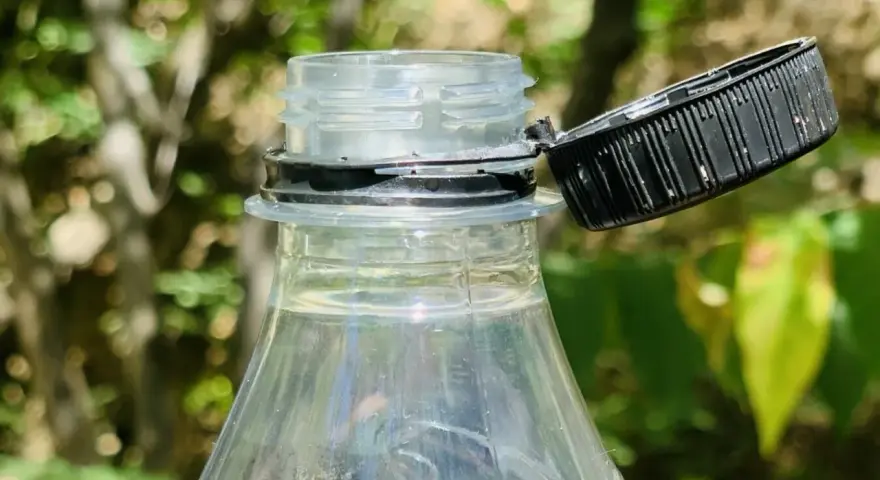 Nakrętki od butelek są przytwierdzone, by zapobiec ich zgubieniu i ułatwić ponowne zakręcenie. Widoczny fragment plastikowej butelki z otwartą, czarną nakrętką.