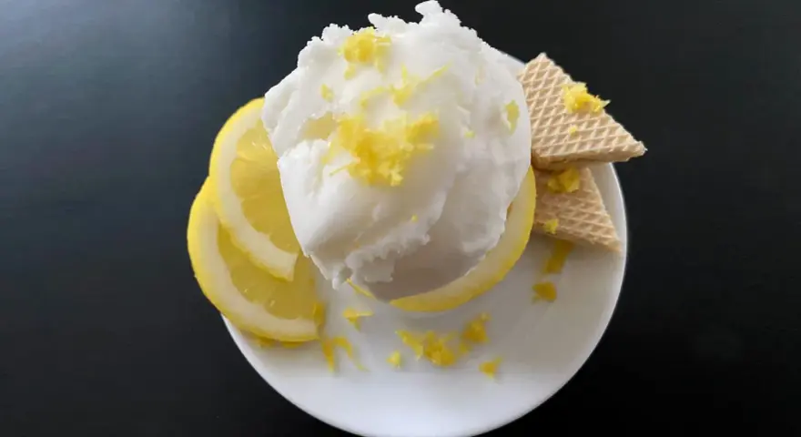 Erfrischendes zitroneneis wie beim Italiener, garniert mit Zitronenschale, Zitronenscheiben und Waffeln auf einem weißen Teller.