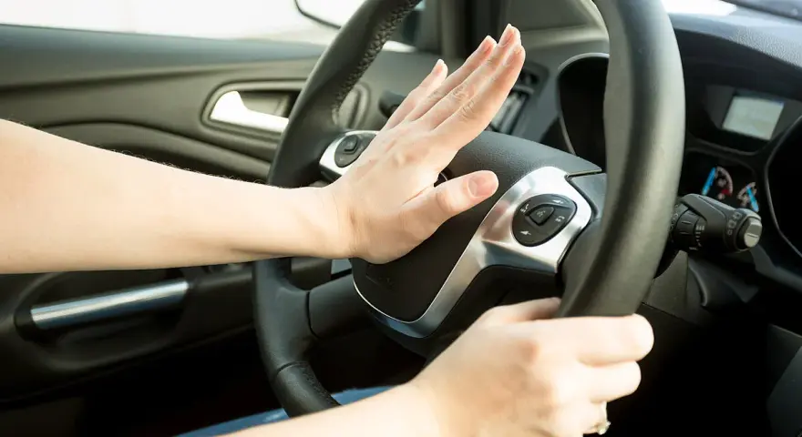 Hand drückt auf Hupe im Auto. Wann darf man hupen? Nur in Notfällen, um einen Unfall zu vermeiden.