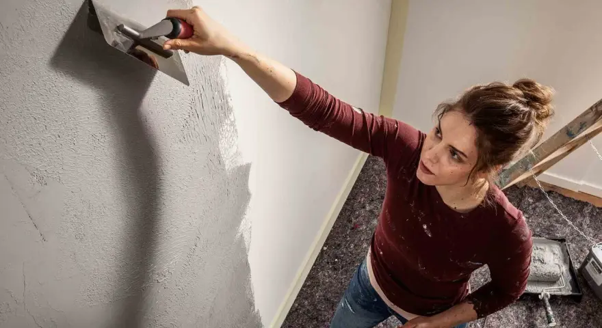 Frau trägt mit einem Spachtel eine Struktur auf die Wand auf. Die Spachteltechnik Wand verleiht dem Raum eine besondere Optik.