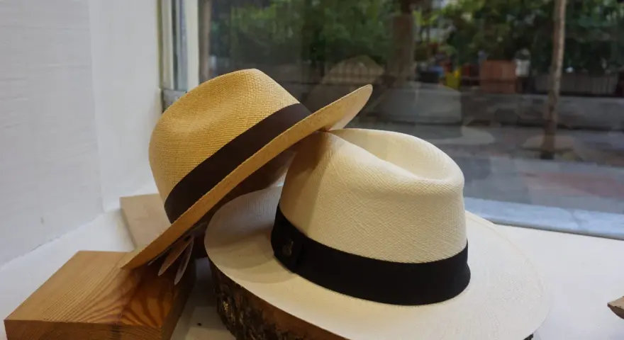 Dos sombreros panameños, uno beige y otro blanco, con cintas oscuras, exhibidos sobre madera y tronco.