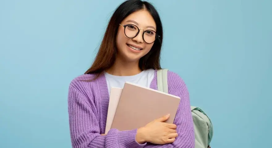 Ragazza con occhiali nuovi per astigmatismo, sorride tenendo libri e zaino.