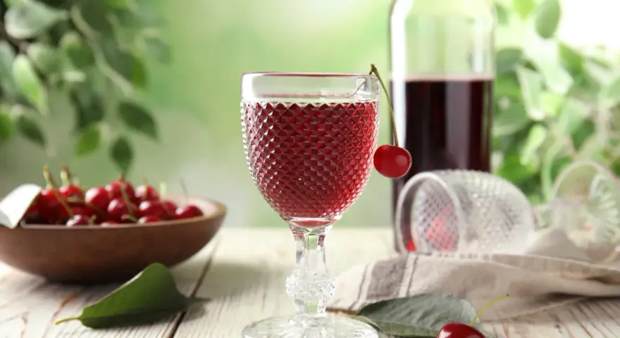 Szklanka z czerwonym winem, wiśnie i butelka. Idealny przepis na wino czerwone z wiśni.
