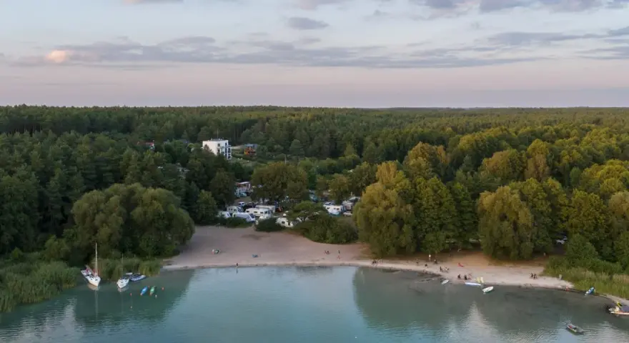 Widok na kemping nad najczystszym jeziorem w Polsce. Woda jest turkusowa, a brzeg piaszczysty. W oddali las.