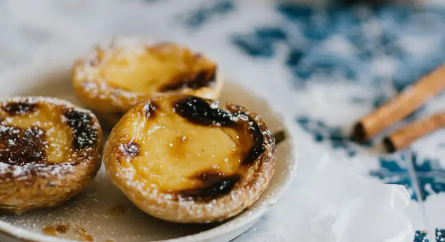 Pastéis de nata, un must per sapere cosa mangiare a Porto. Dolci cremosi su un piatto, spolverati di zucchero a velo, con cannella sullo sfondo.