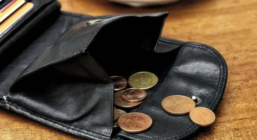 Schwarzes Lederportemonnaie mit Münzen. Die wenigen Münzen symbolisieren die Opportunitätskosten, wenn man sich für eine Ausgabe entscheidet.