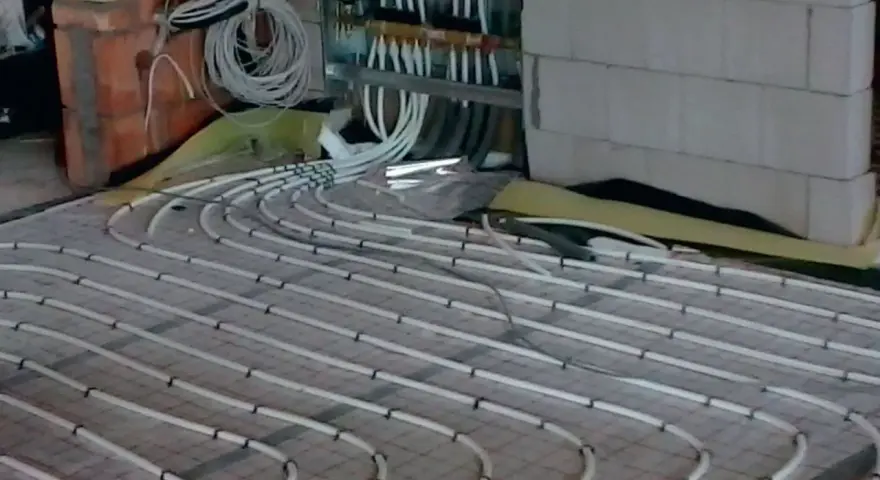 Instalacja ogrzewania podłogowego. Rury ułożone na siatce, podłączone do rozdzielacza. To rozwiązanie obniża koszt ogrzewania.