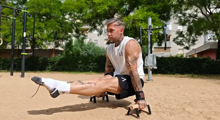 Un homme musclé exécute un exercice de calisthenics, jambes tendues, dans un parc. Un entraînement complet pour un corps athlétique.