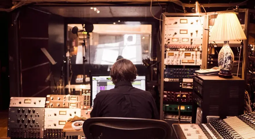 Osoba siedzi przed komputerem w profesjonalnym **recording studio**, otoczona sprzętem audio i mikserem.