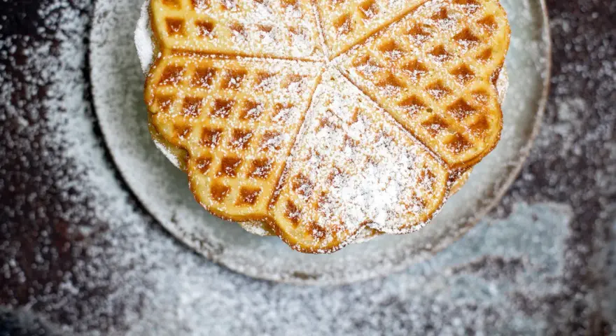 Herzförmige Waffeln, bestäubt mit Puderzucker, auf einem Teller. Ein köstliches Rezept für süße Momente.