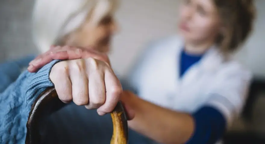 Opiekunka wspiera starszą panią, która trzyma laskę. Zastanawiasz się, ile kosztuje opiekunka z mops?