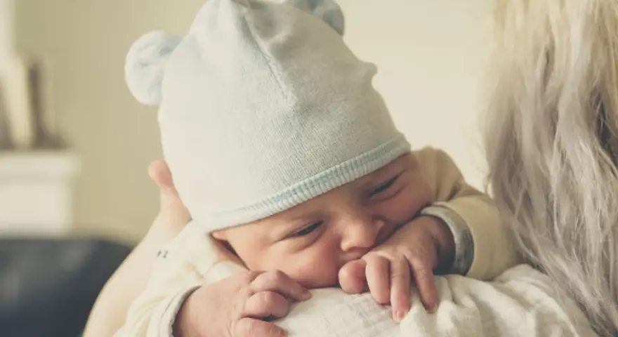 Nyfödd bebis med mössa med öron, tryggt vilande mot en axel. En perfekt baby gåva.