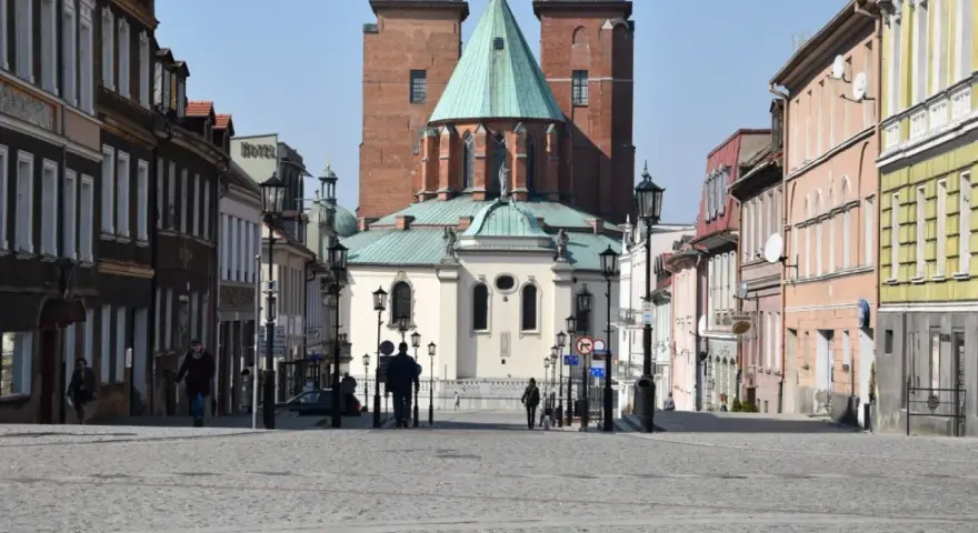 Spacer po brukowanym rynku Gniezna, z katedrą w tle. Kolorowe kamienice po bokach tworzą urokliwą atmosferę.