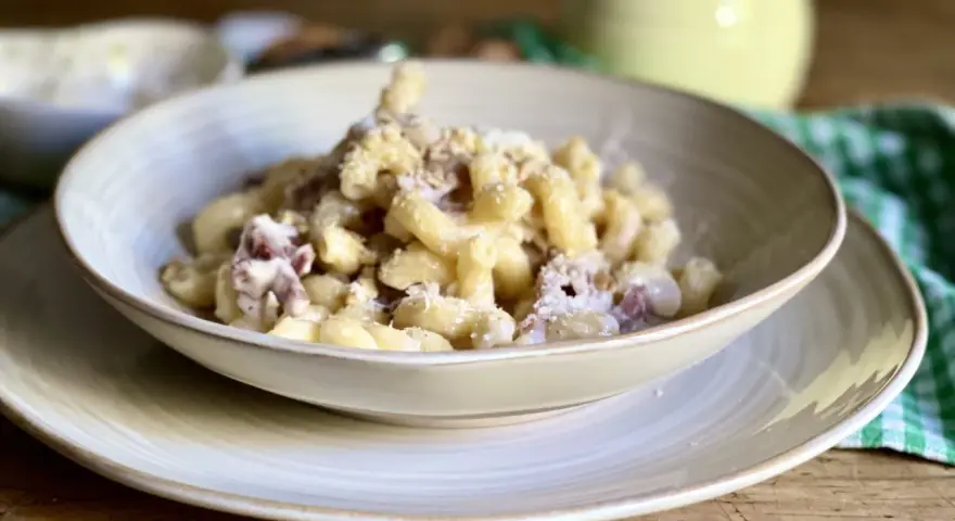 Piatto di pasta con prosciutto crudo, formaggio grattugiato e una salsa cremosa. Un classico confortante.