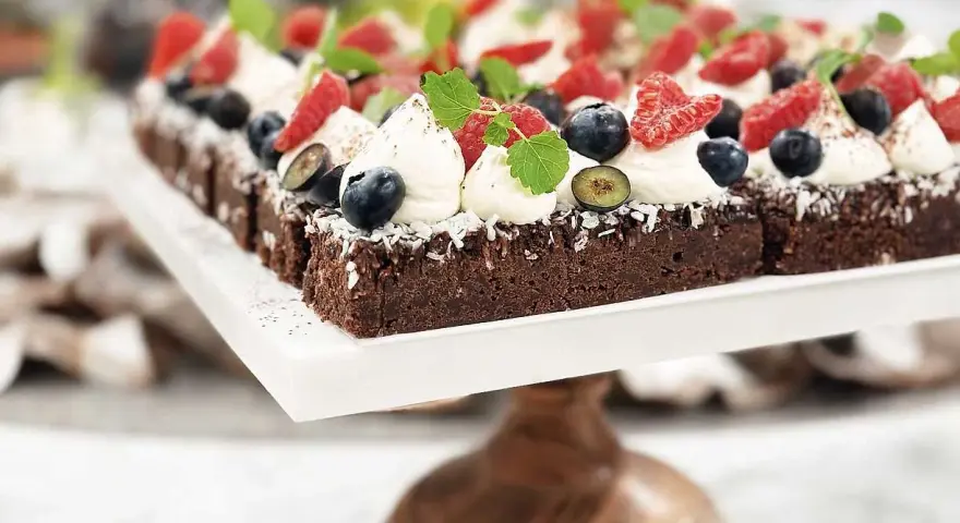 En rad läckra bitar kladdkaka med fudge, toppade med vispad grädde, färska bär och mynta.