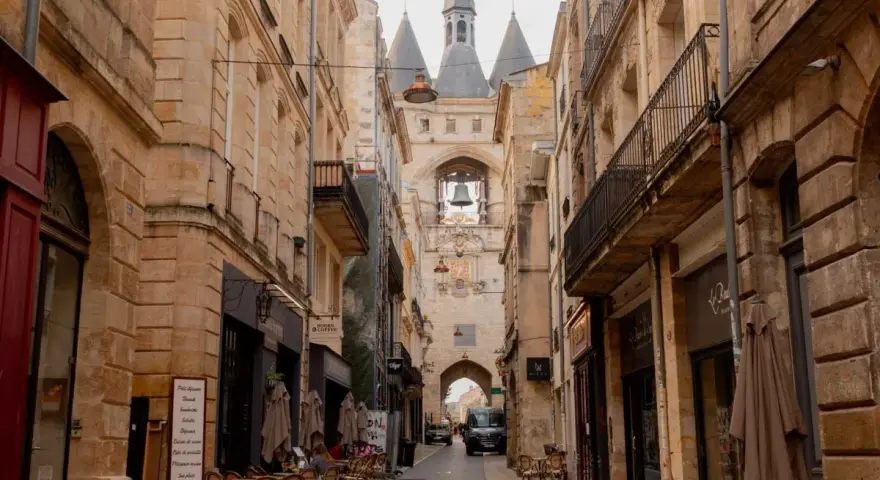 A charming street in Bordeaux leads to the iconic Grosse Cloche bell tower. Cafes and shops line the cobblestone path, making you wonder, is Bordeaux worth visiting? Absolutely!