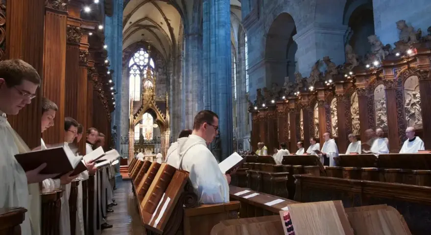 Men in white robes read from books in a grand cathedral, likely participating in matins, a morning prayer service.