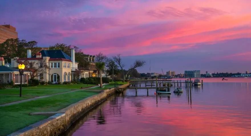Beautiful waterfront homes and boats reflect a vibrant pink and purple sunset, perfect for weekend trips from Richmond, VA.