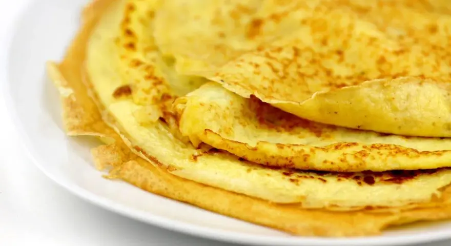 Ein Stapel goldbrauner Eierkuchen auf einem weißen Teller. Perfekt für ein schnelles und einfaches Eierkuchen Rezept.
